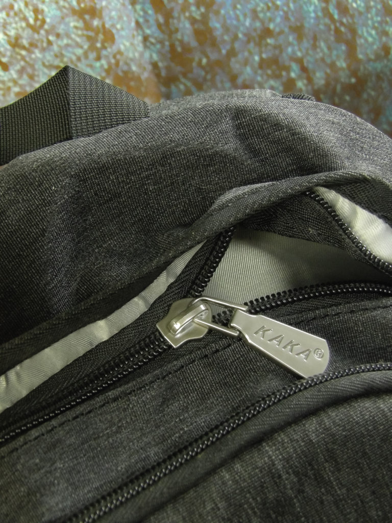 The primary zipper is discretely concealed by a fabric pleat